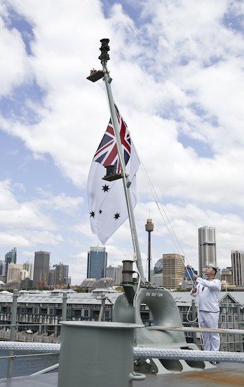 Leading Seaman Stewart Thurlow raises the Australian White Ensign onboard HMAS Canberra during the commissioning ceremony. (Defence)