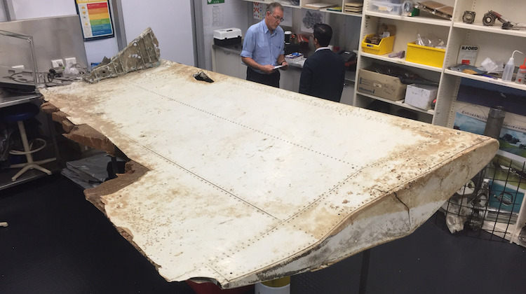 A supplied image of ATSB investigators looking at a wing flap believed to be from MH370. (ATSB)