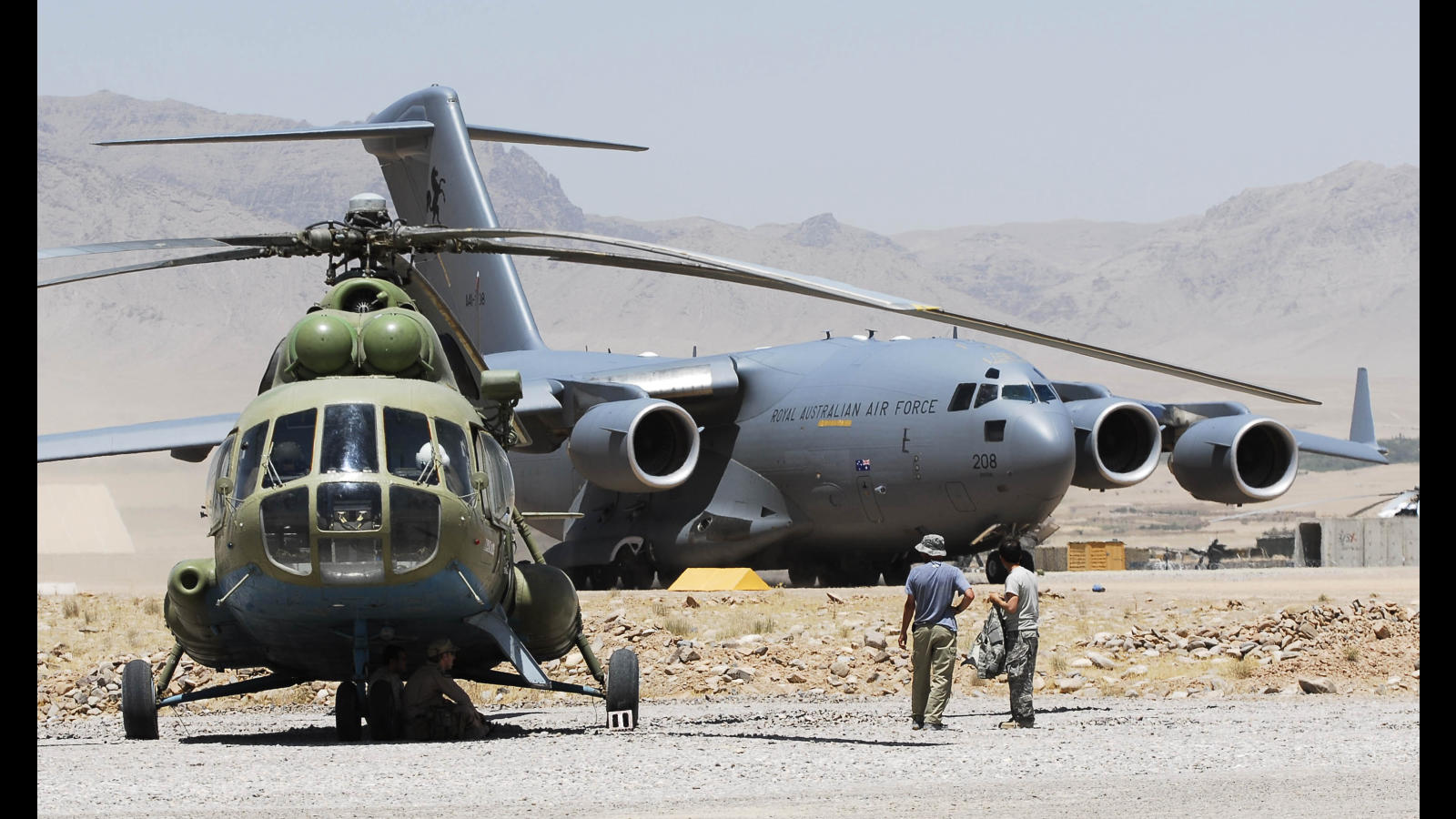 An Australian C-17 Globemaster looms large over a Russian made Mi-8 HIP helicopter on the dusty parking apron at Tarin Kowt in Afghanistan. Mid Caption: The Air Load Team is responsible for the safe and timely loading and unloading of cargo from Australian and Coalition aircraft in locations throughout the Operation Slipper area of operations. Operation SLIPPER is Australia's military contribution to coalition efforts against international terrorism. Under this operation our forces contribute to the efforts of the North Atlantic Treaty Organisation (NATO) - led International Security Assistance Force in Afghanistan, aimed at preventing Afghanistan again becoming a safe haven for international terrorists, and the United States-led International Coalition Against Terrorism (ICAT) efforts in the broader Middle East.